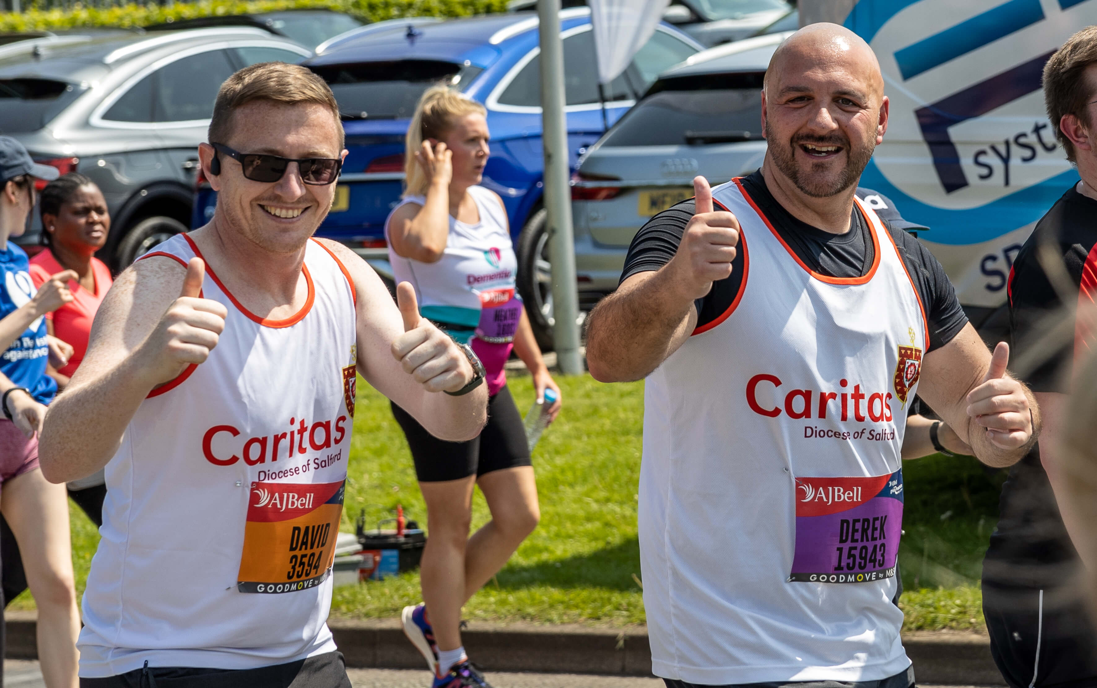 Two people in white Caritas running vests smiling at camera while running and giving thumbs up sign