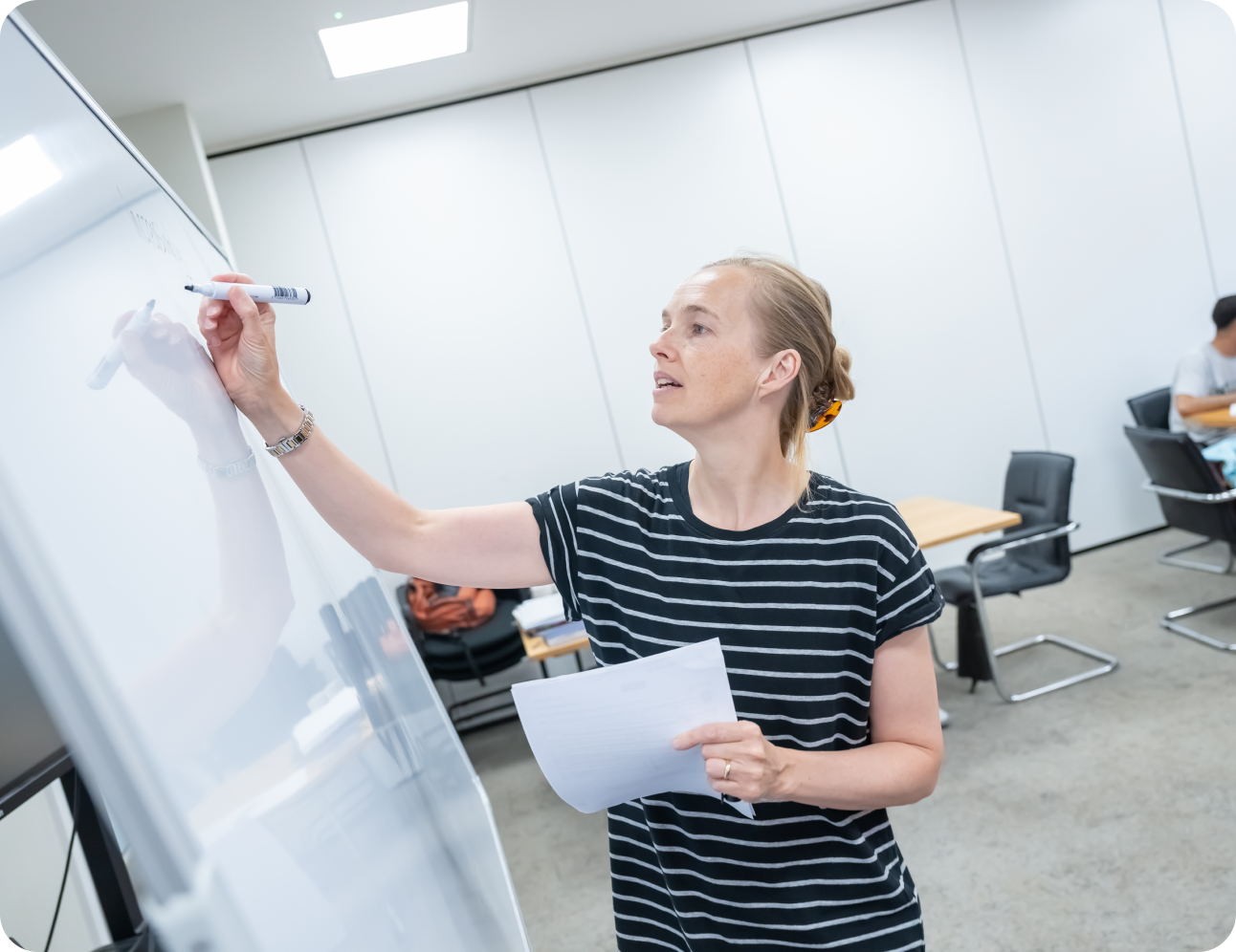 training business lady in striped tshirt writing on board with pen and holding paper