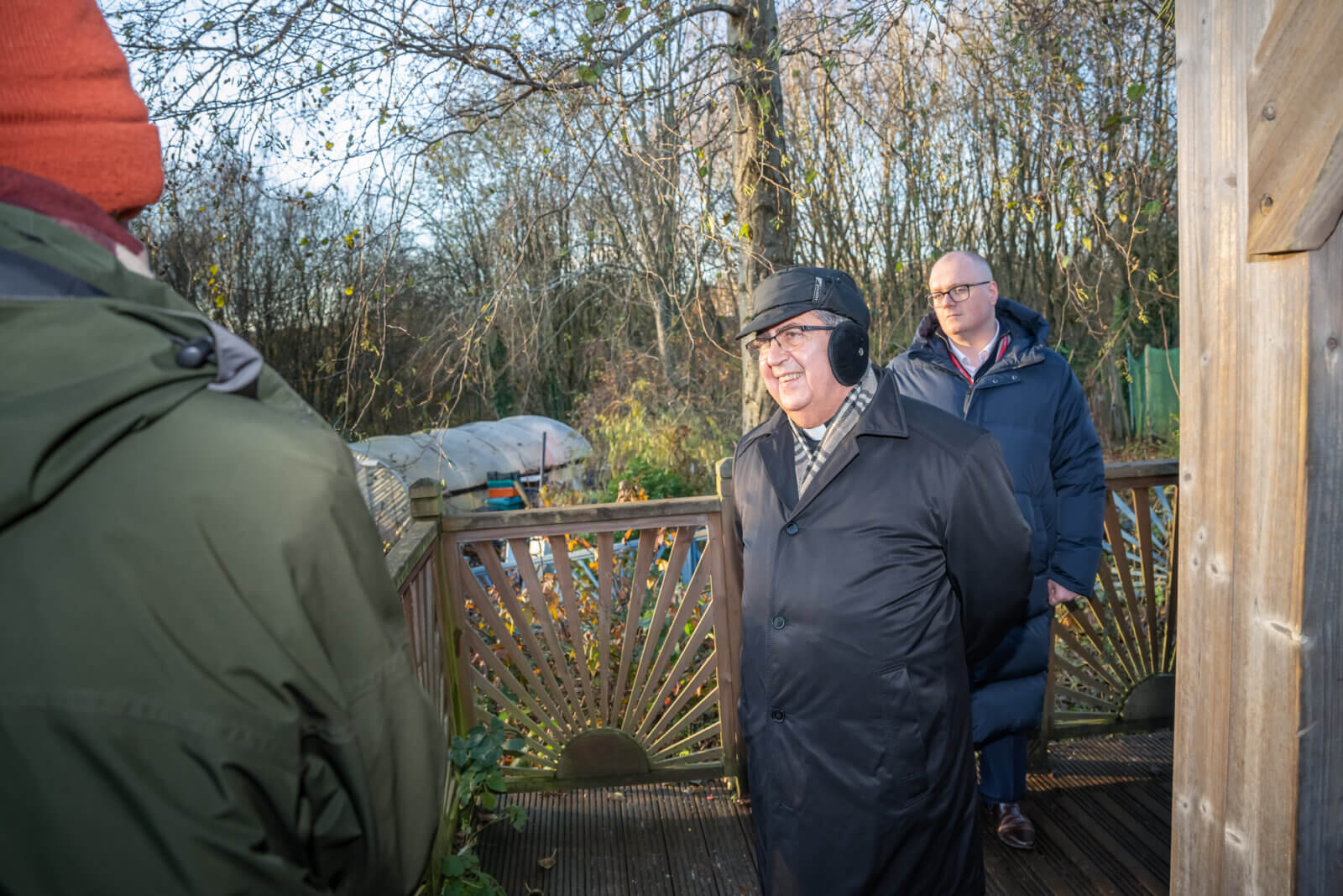Nuncio in black goad and hat smiling at someone off camera. Caritas Salford allotment in background