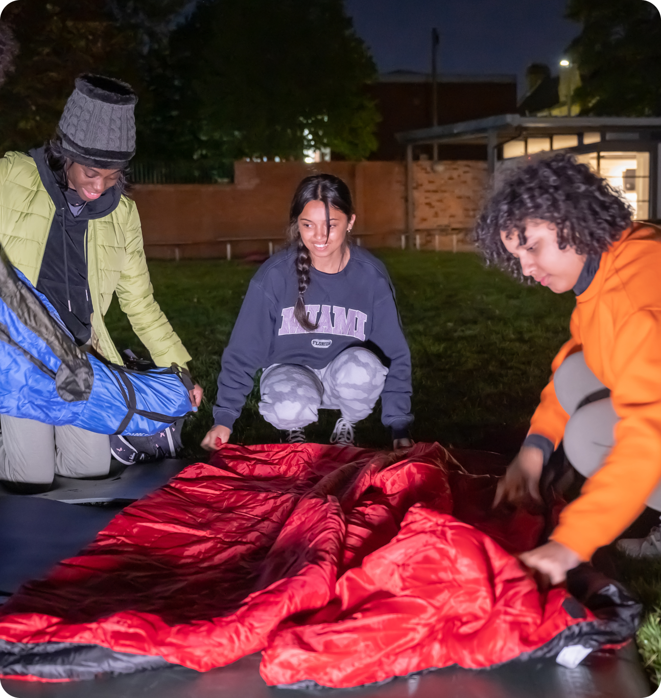 Four people laying out a red sleeping bag on the ground for the big sleep out