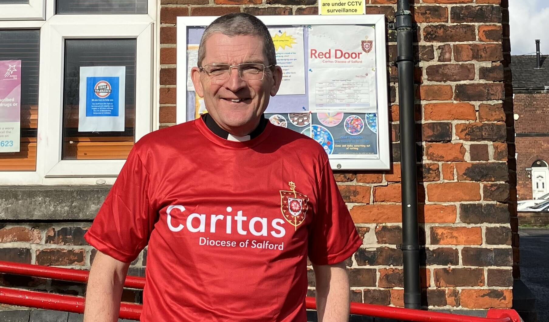 Man smiling at camera wearing a red Caritas Salford tshirt