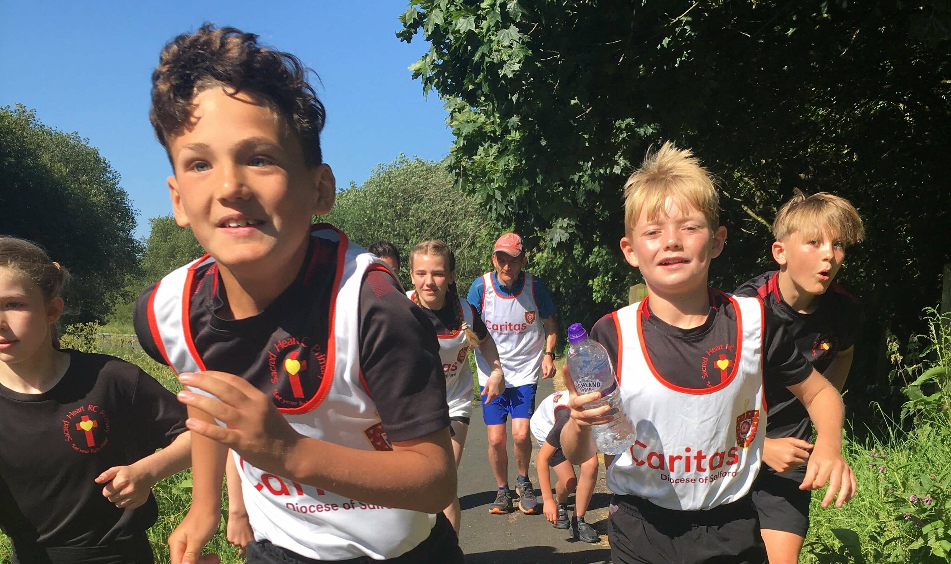 Children in white Caritas vests running along canal path