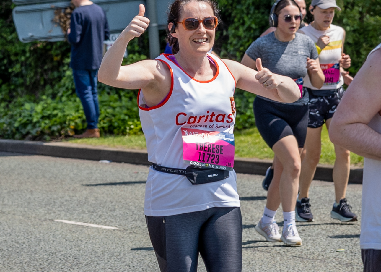 lady running in white vest with caritas logo on it holding up thumbs at camera and smiling