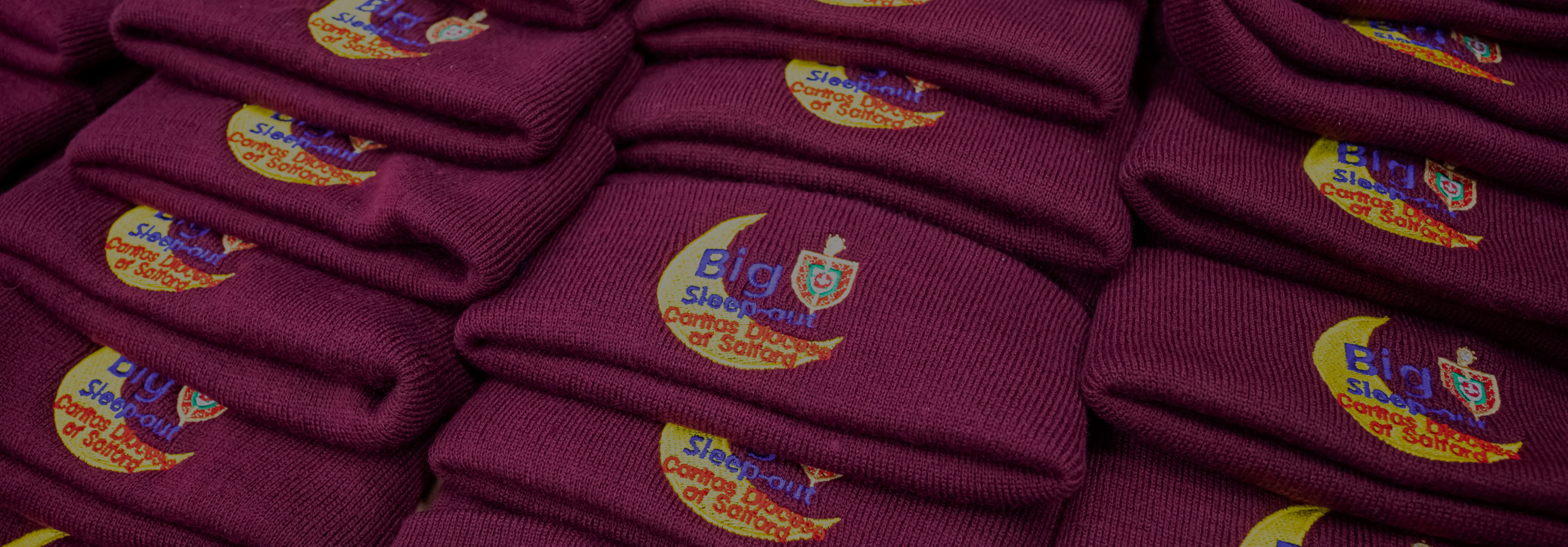 Close-up-of-pile-of-dark-red-hats-with-the-Caritas-big-sleep-out-logo