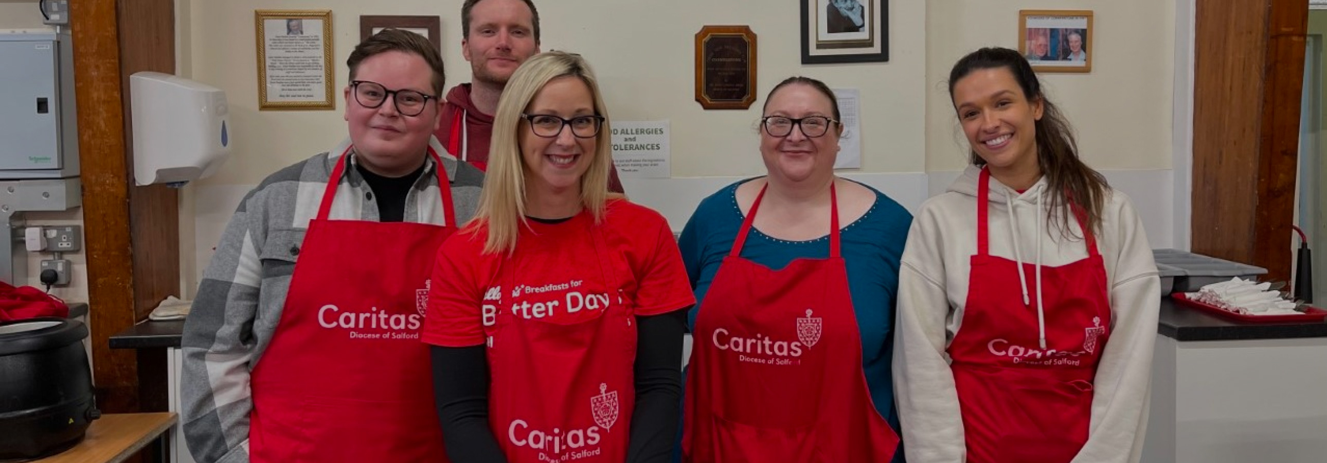 Group-of-corporate-volunteers-in-line-smiling-at-camera-all-wearing-red-caritas-aprons