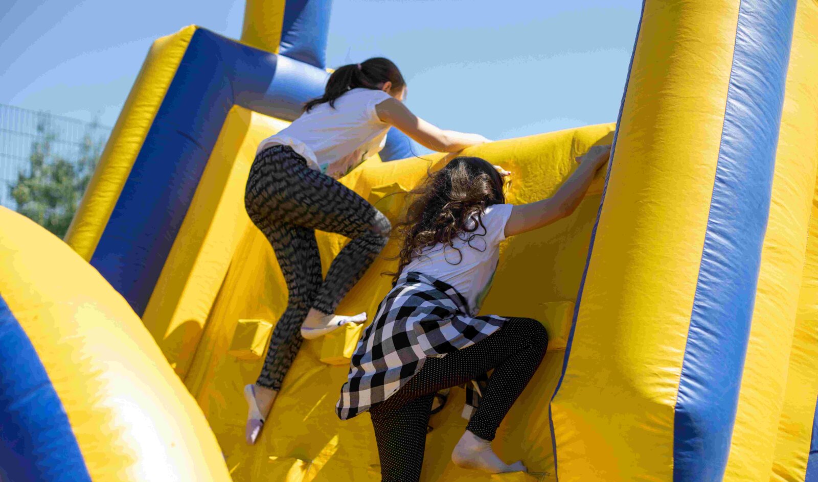 Two girls climbing over yellow and blue inflatable obstacle