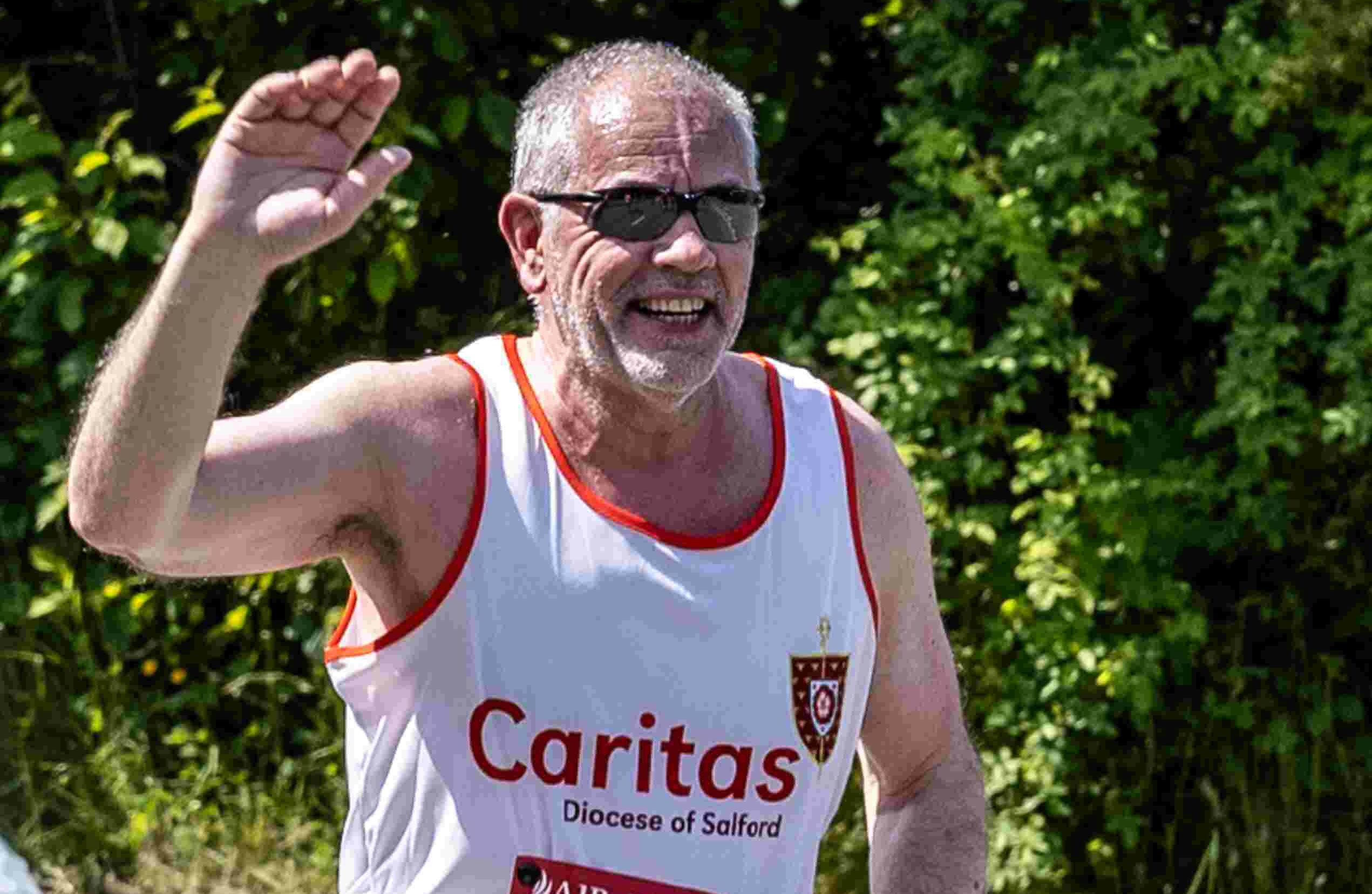 Man running in white vest with Caritas logo on it, waving at camera