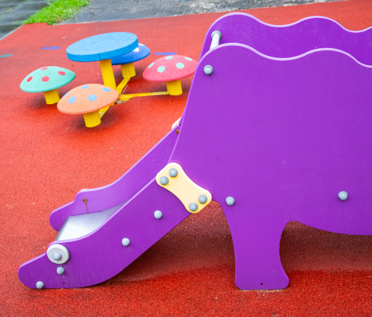 red playground with a close up of a purple slide and a brightly coloured childs chair and table in shape of mushrooms