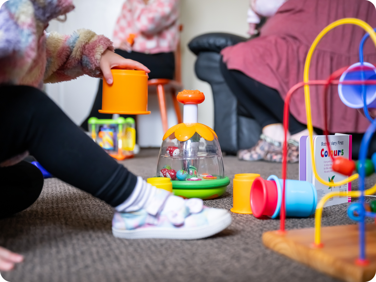 childs leg in black leggings and white trainers with toys on carpet