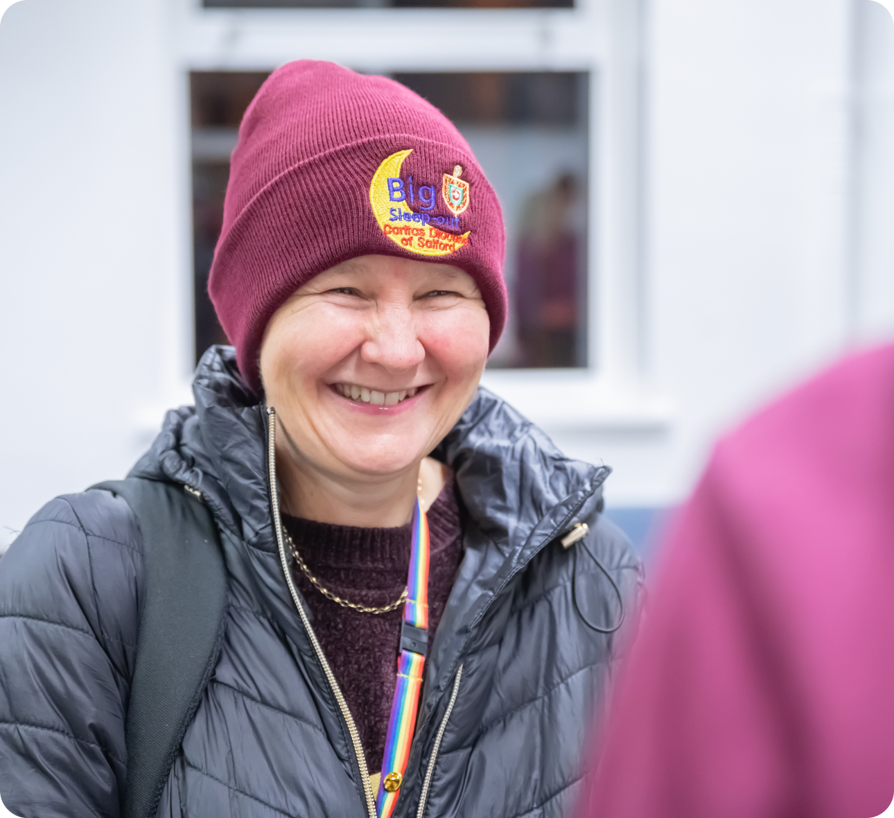 person in dark red big sleep out branded woollen hat and black padded coat smiling
